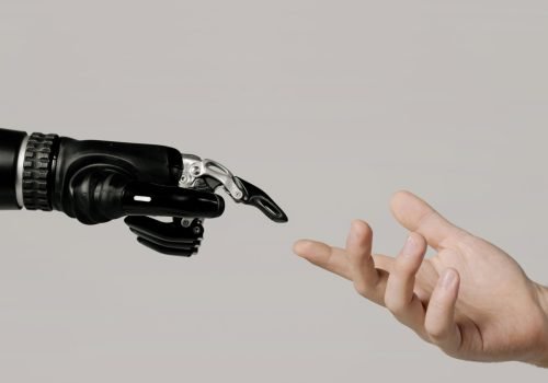 pexels-photo-6153343-6153343 A human hand reaching to touch a bionic prosthetic hand on a white background.